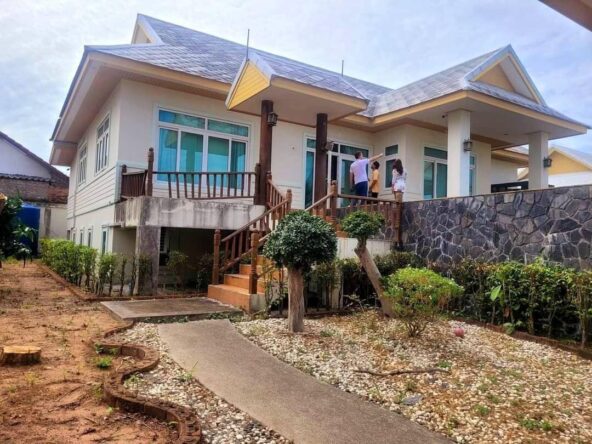 Exterior view of a spacious 7-bedroom house in Baan Amorn Village, featuring a modern design and lush greenery.